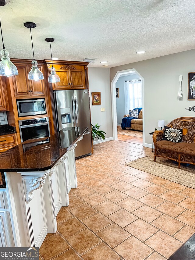 kitchen featuring a textured ceiling, stainless steel appliances, dark stone countertops, hanging light fixtures, and light tile patterned flooring