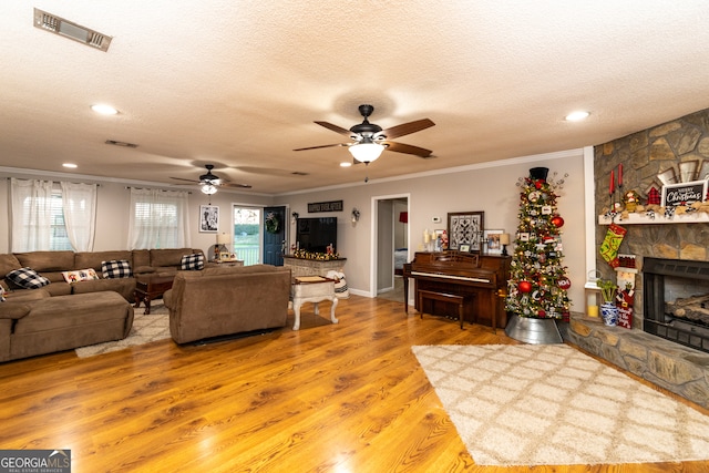 living room featuring crown molding, hardwood / wood-style flooring, ceiling fan, a fireplace, and a textured ceiling