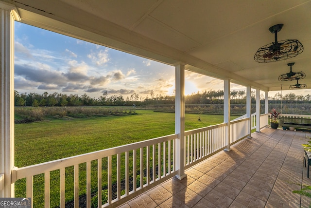 deck at dusk featuring a lawn, a rural view, and a porch