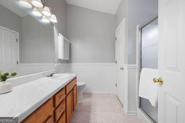 bathroom with tile patterned floors, vaulted ceiling, toilet, a shower with door, and vanity