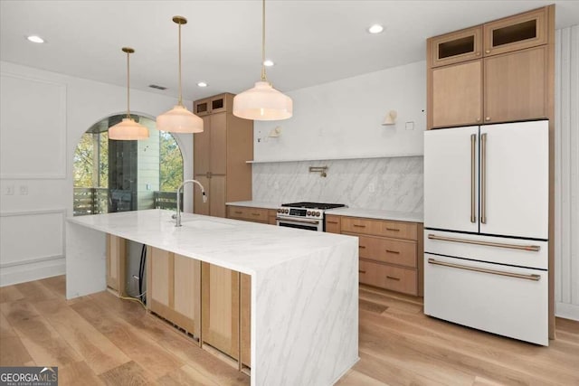 kitchen with a center island with sink, white refrigerator, light hardwood / wood-style flooring, and stainless steel range with gas stovetop