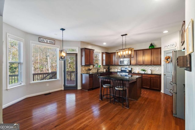 kitchen with a breakfast bar, a kitchen island, dark hardwood / wood-style floors, and appliances with stainless steel finishes