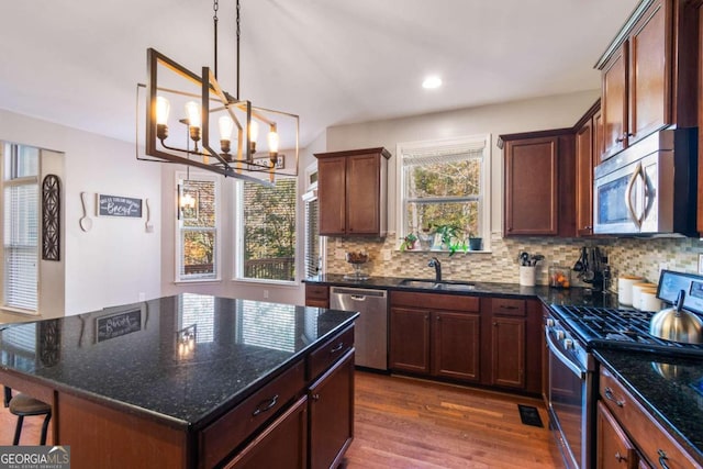 kitchen with stainless steel appliances, dark wood-type flooring, an inviting chandelier, dark stone countertops, and a center island