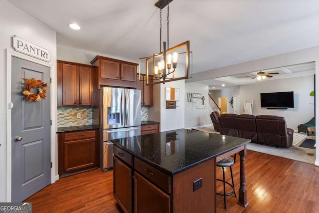 kitchen with dark hardwood / wood-style flooring, dark stone countertops, stainless steel fridge, a breakfast bar, and a kitchen island