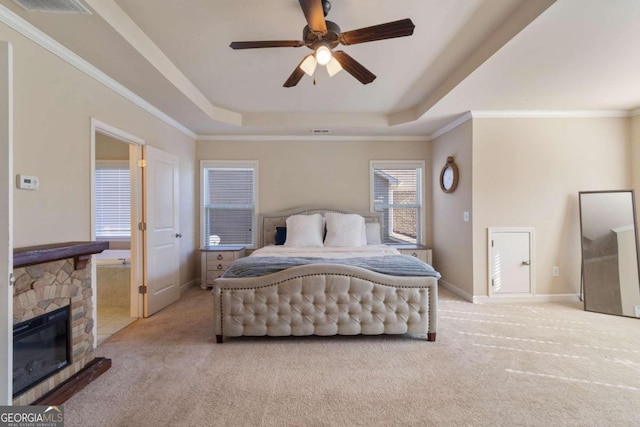 carpeted bedroom with a raised ceiling, a stone fireplace, ceiling fan, and ornamental molding