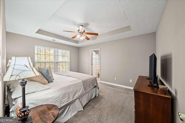 carpeted bedroom with ceiling fan, ensuite bath, and a tray ceiling