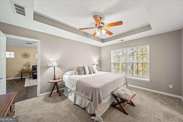 bedroom with ceiling fan, dark carpet, and a raised ceiling