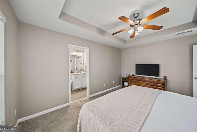 bedroom with light colored carpet, ceiling fan, a tray ceiling, and ensuite bathroom