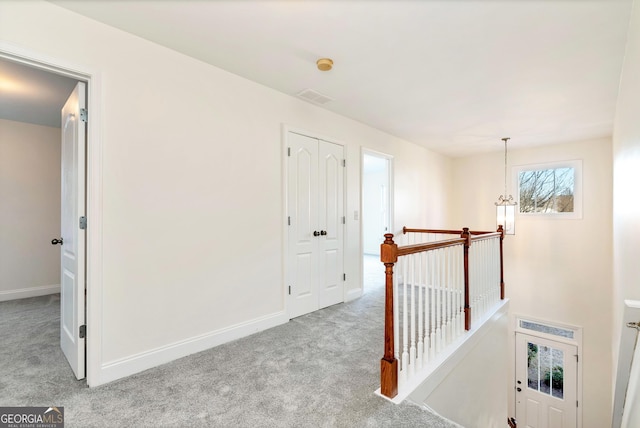 hallway with light colored carpet and a notable chandelier