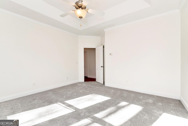 empty room with a raised ceiling, ceiling fan, crown molding, and carpet flooring