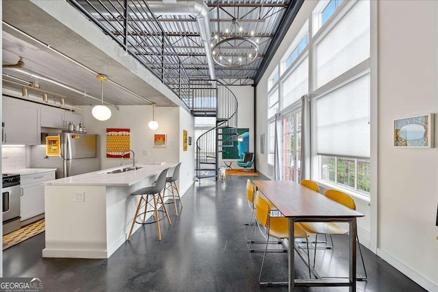 kitchen featuring pendant lighting, sink, stainless steel refrigerator, stove, and a towering ceiling