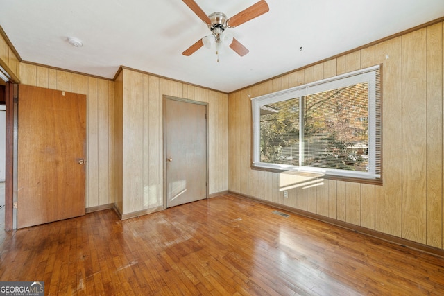 unfurnished bedroom featuring ceiling fan, wood walls, wood-type flooring, and a closet