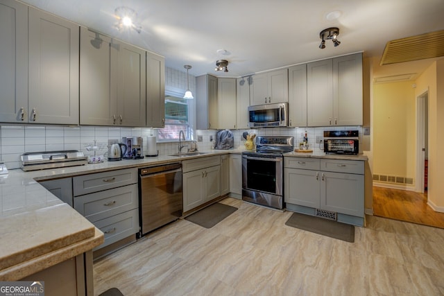 kitchen with gray cabinetry, backsplash, sink, appliances with stainless steel finishes, and decorative light fixtures