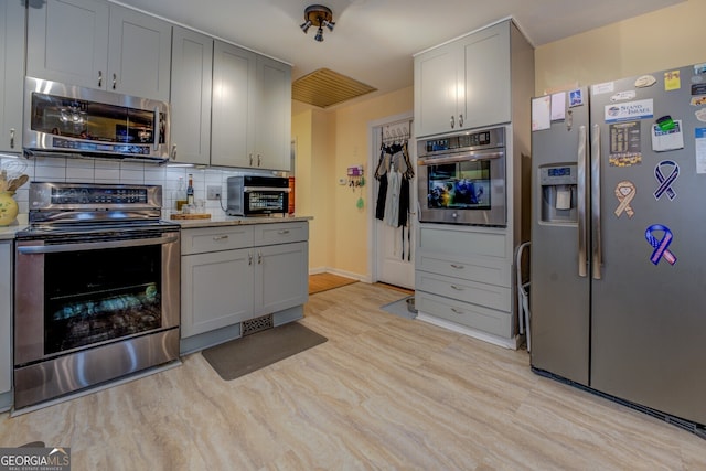 kitchen with tasteful backsplash, gray cabinetry, stainless steel appliances, and light hardwood / wood-style floors