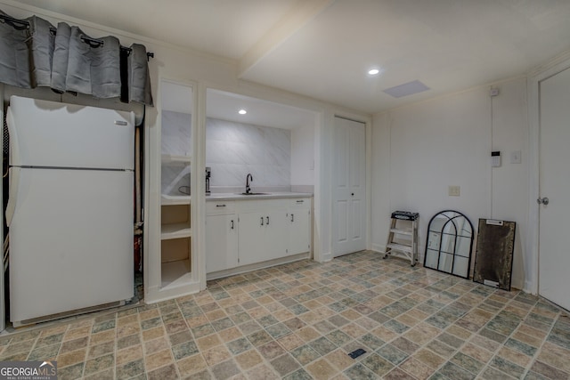 kitchen with white refrigerator, white cabinetry, and sink