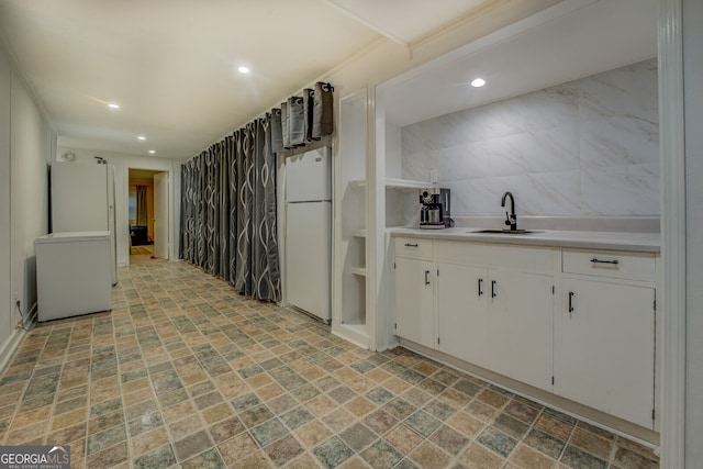 kitchen featuring white refrigerator, white cabinetry, tile walls, and sink