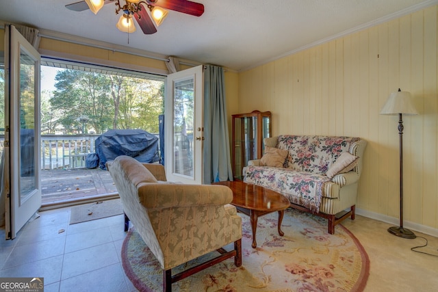 sitting room featuring ceiling fan, wooden walls, light tile patterned flooring, and ornamental molding