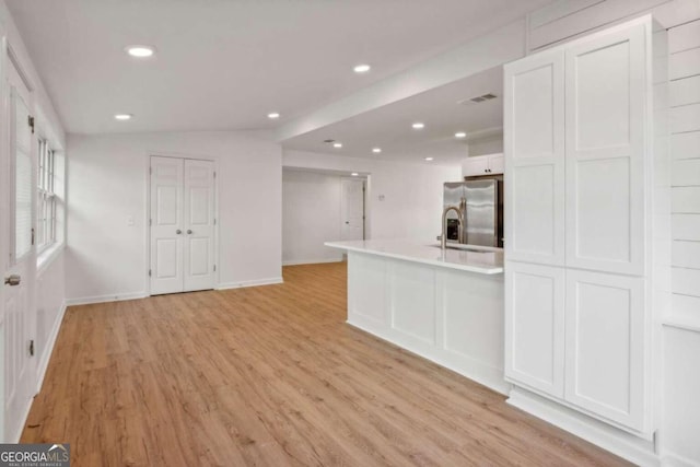 kitchen with stainless steel fridge, sink, white cabinets, light hardwood / wood-style floors, and lofted ceiling