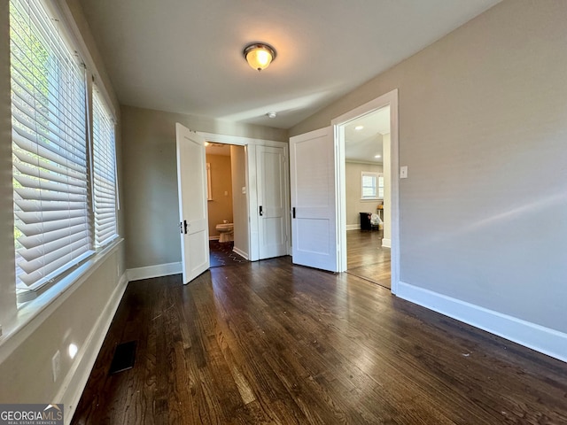 unfurnished bedroom featuring ensuite bath, multiple windows, and dark hardwood / wood-style floors