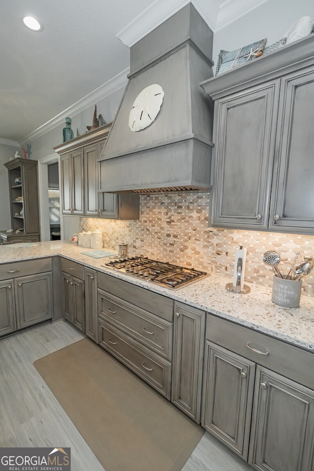 kitchen featuring backsplash, premium range hood, stainless steel gas stovetop, and crown molding