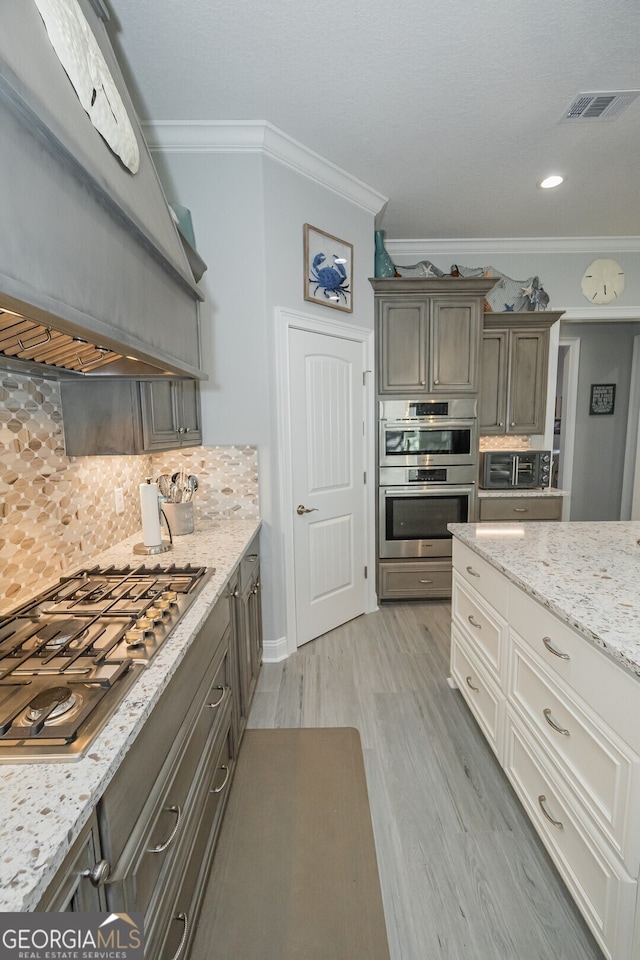 kitchen with stainless steel appliances, tasteful backsplash, light hardwood / wood-style floors, white cabinets, and ornamental molding