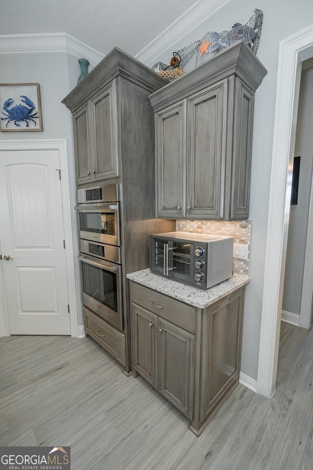 kitchen featuring light stone counters, stainless steel double oven, light wood-type flooring, and ornamental molding