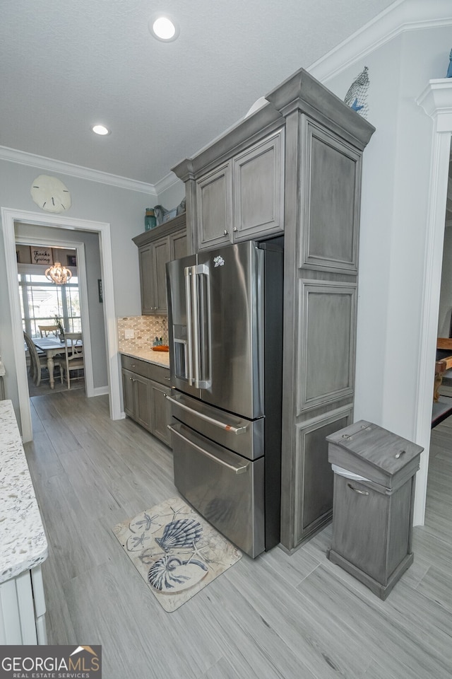 kitchen with high end refrigerator, light stone counters, light hardwood / wood-style floors, decorative backsplash, and ornamental molding