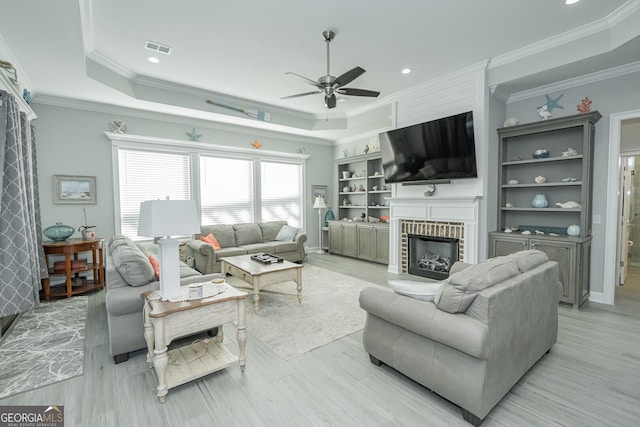 living room with crown molding, a fireplace, ceiling fan, and light wood-type flooring