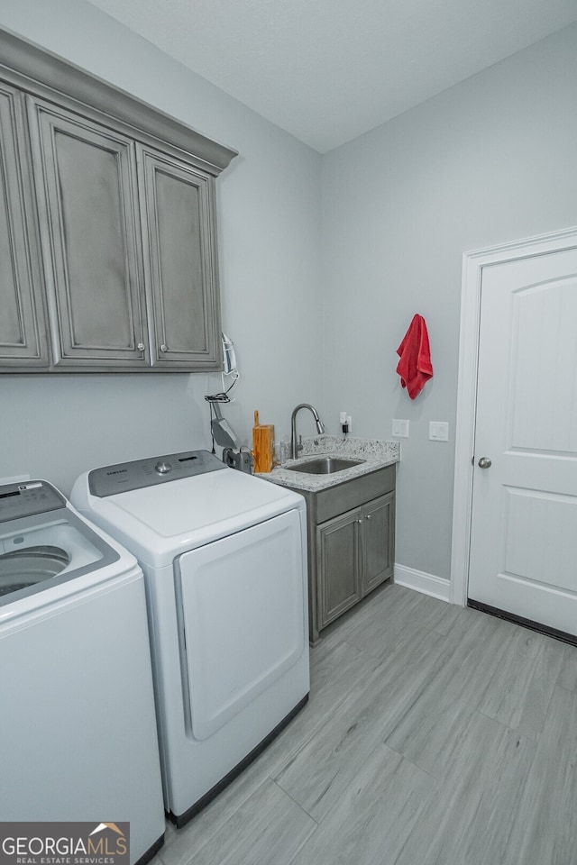 clothes washing area with cabinets, light hardwood / wood-style flooring, washing machine and clothes dryer, and sink