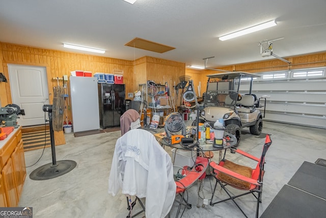 garage with black fridge, wooden walls, a garage door opener, and white refrigerator