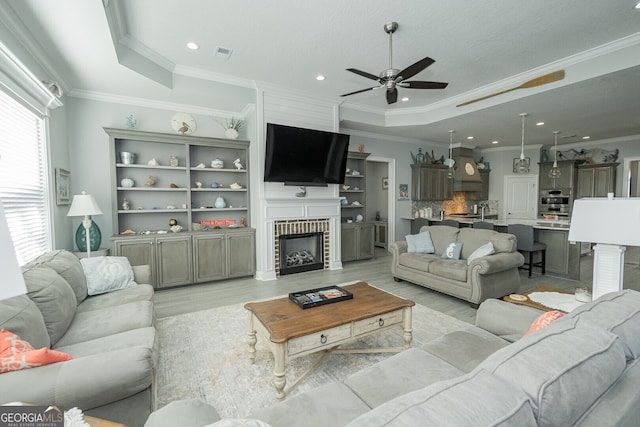 living room featuring ceiling fan, a raised ceiling, ornamental molding, and light hardwood / wood-style flooring