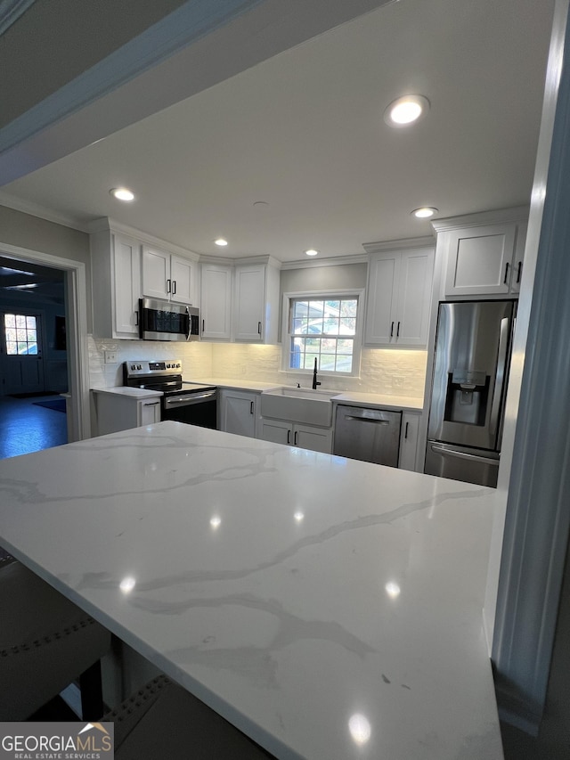 kitchen featuring light stone countertops, stainless steel appliances, crown molding, sink, and white cabinets