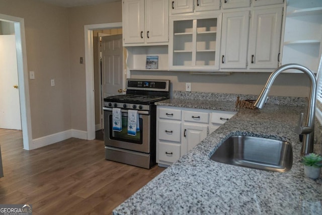 kitchen featuring stainless steel gas range oven, white cabinetry, sink, and hardwood / wood-style floors