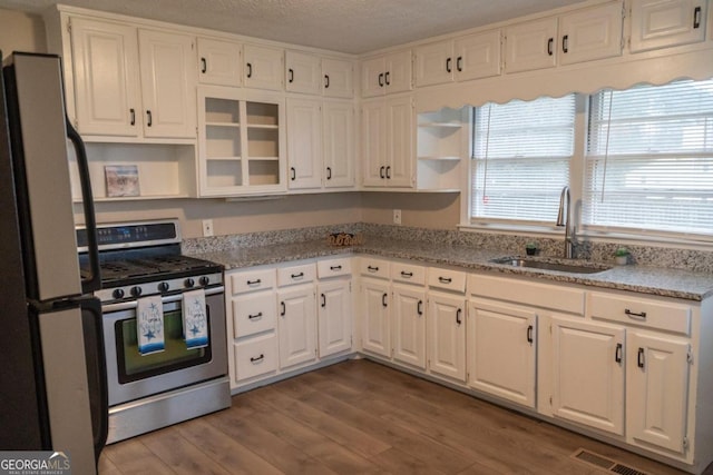 kitchen with sink, stainless steel range oven, white refrigerator, wood-type flooring, and white cabinets