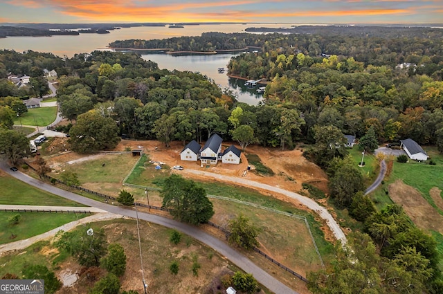 aerial view at dusk with a water view and a view of trees