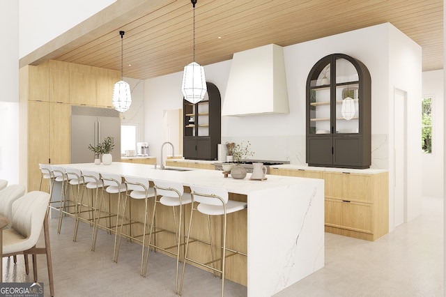 kitchen with built in fridge, range hood, wood ceiling, and a large island with sink