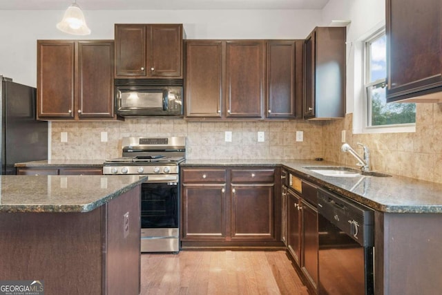 kitchen with pendant lighting, dark stone counters, black appliances, sink, and light hardwood / wood-style flooring