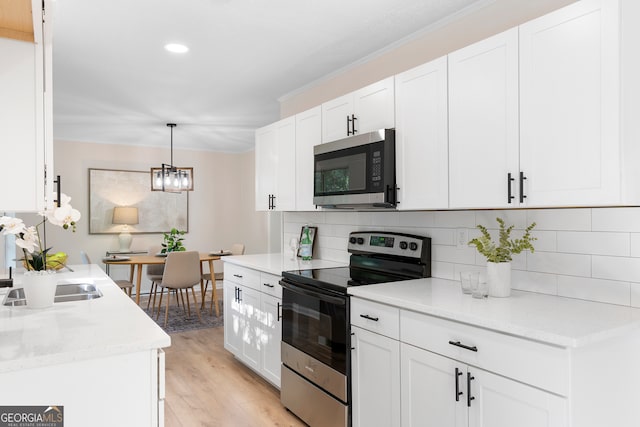 kitchen featuring backsplash, white cabinets, light wood-type flooring, appliances with stainless steel finishes, and decorative light fixtures