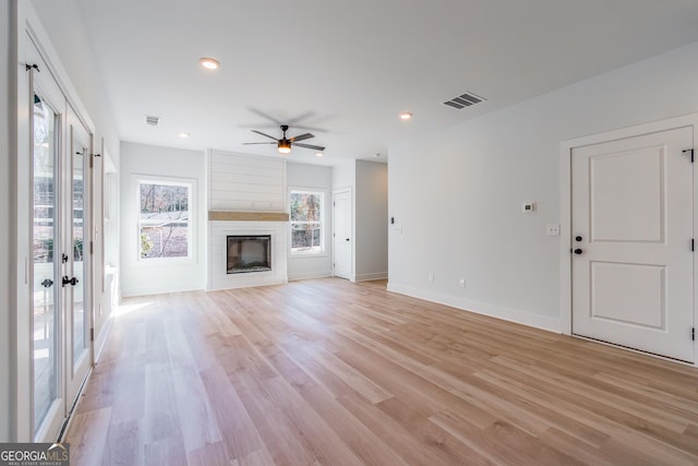 unfurnished living room with ceiling fan, a large fireplace, and light hardwood / wood-style flooring