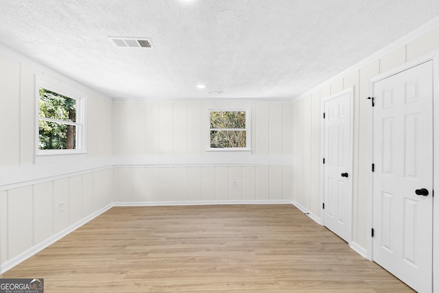 spare room with plenty of natural light, a textured ceiling, and light hardwood / wood-style flooring