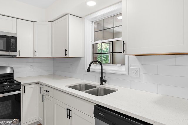 kitchen with light stone countertops, sink, stainless steel appliances, backsplash, and white cabinets