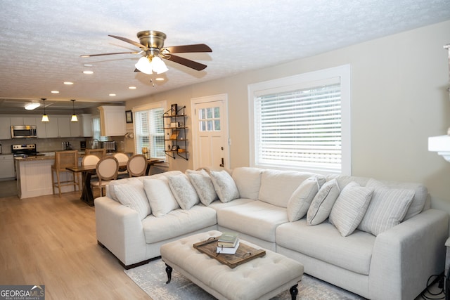 dining space featuring a textured ceiling, light hardwood / wood-style floors, a brick fireplace, and ceiling fan