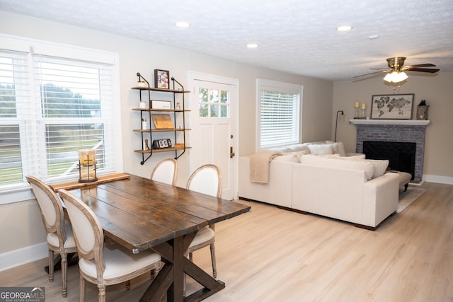 dining area with ceiling fan, a brick fireplace, a textured ceiling, and light wood-type flooring