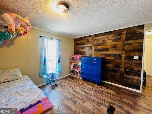 bedroom with dark hardwood / wood-style flooring, ornamental molding, a textured ceiling, and wooden walls