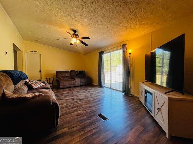 living room featuring ceiling fan, dark wood-type flooring, and a textured ceiling