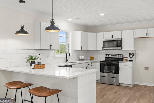 kitchen with kitchen peninsula, appliances with stainless steel finishes, sink, pendant lighting, and white cabinets