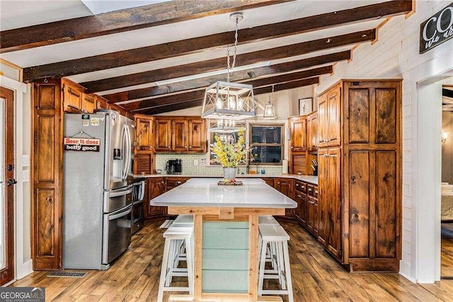 kitchen featuring stainless steel refrigerator with ice dispenser, a breakfast bar, light hardwood / wood-style floors, a kitchen island, and hanging light fixtures