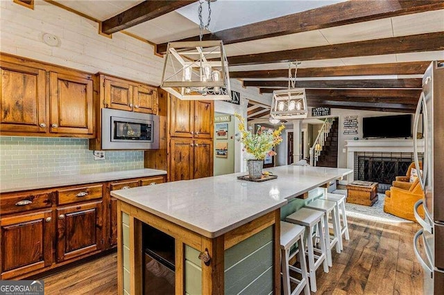 kitchen with a center island, a brick fireplace, pendant lighting, a breakfast bar area, and appliances with stainless steel finishes