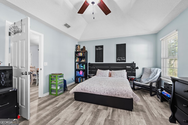 bedroom with wood-type flooring, a textured ceiling, vaulted ceiling, and ceiling fan