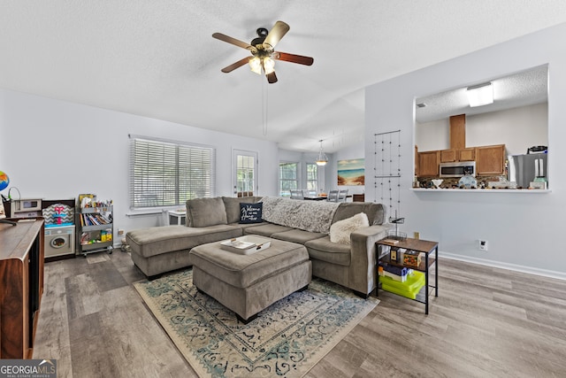 living room with hardwood / wood-style flooring, ceiling fan, lofted ceiling, and a textured ceiling